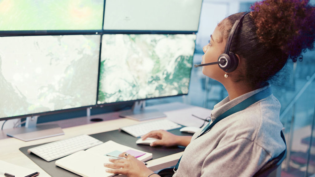 Mulher olhando para grandes telas e fazendo o monitoramento da localização de veículos