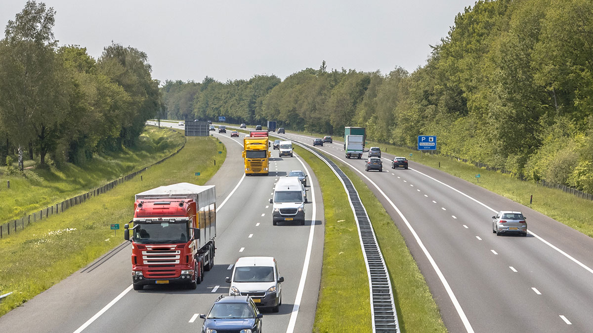 Rodovia movimentada com carros e caminhões cercada por árvores