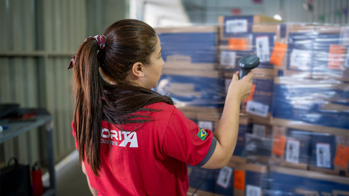 Mulher fazendo leitura de código de barras de pacotes em centro logístico mostrando o processo de Gestão de Inventário
