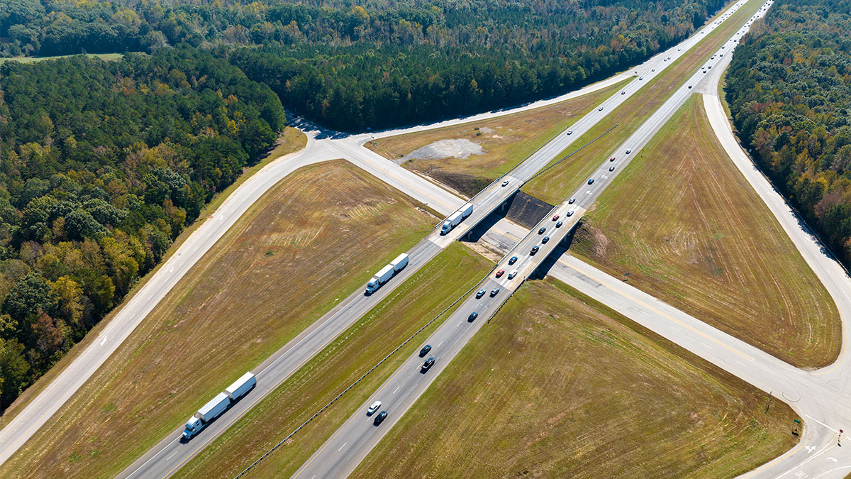 Vista aérea de rodovia com caminhões e carros, ilustrando curiosidades no transporte de cargas.