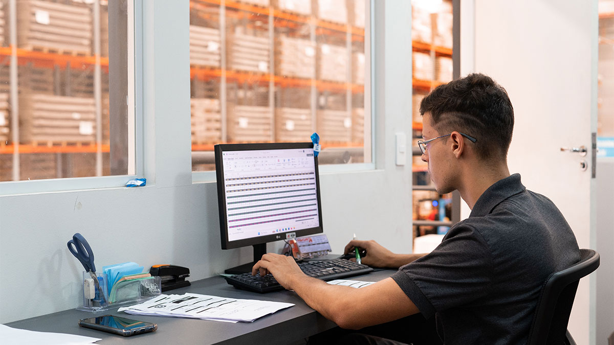 Colaborador da Favorita Transportes analisando planilhas em computador no centro de distribuição, destacando a gestão de logística integrada e a importância do operador logístico.