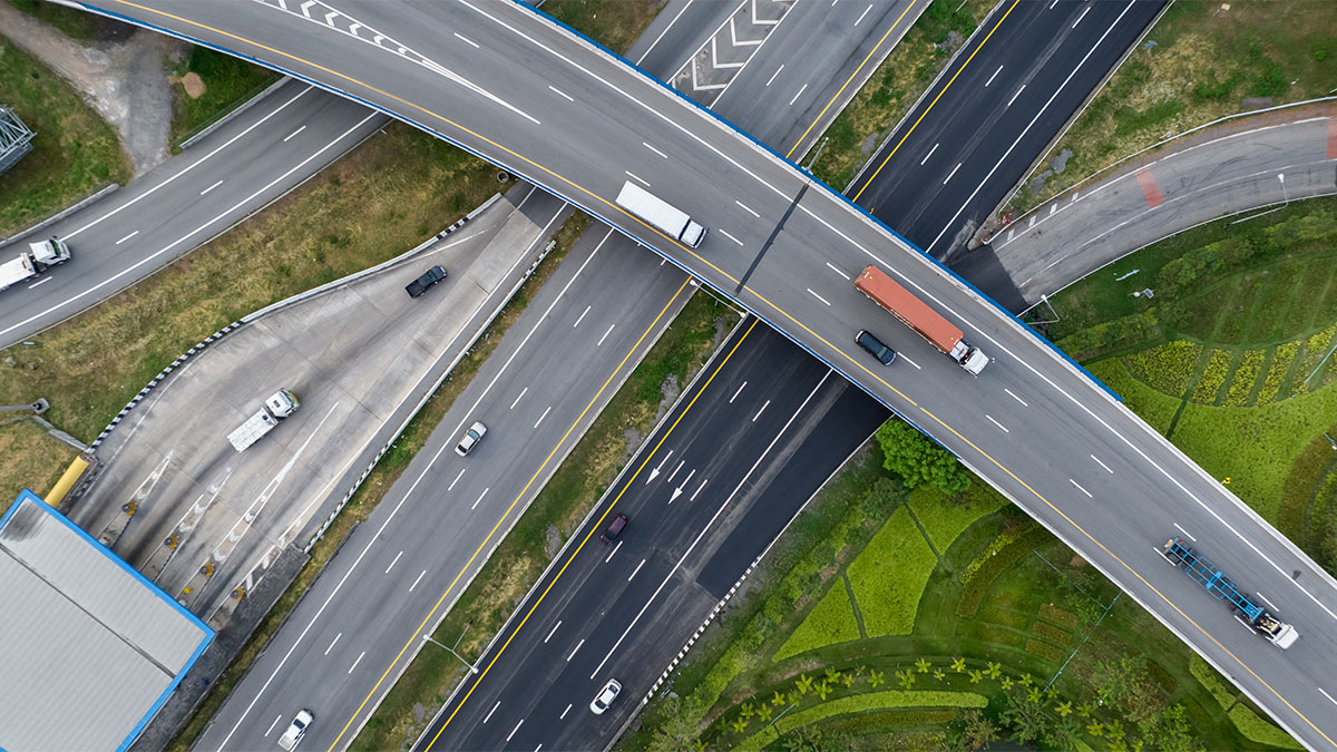 Vista aérea de rodovias com caminhões em trânsito, ilustrando o transporte rodoviário de cargas e a logística eficiente no deslocamento de mercadorias.