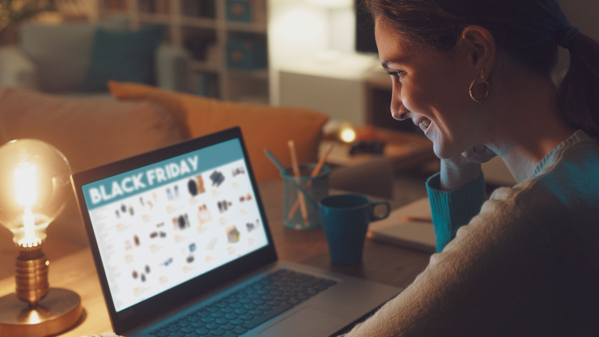 Mulher sorridente faz compras online no notebook durante a Black Friday Brasil, aproveitando promoções no e-commerce.