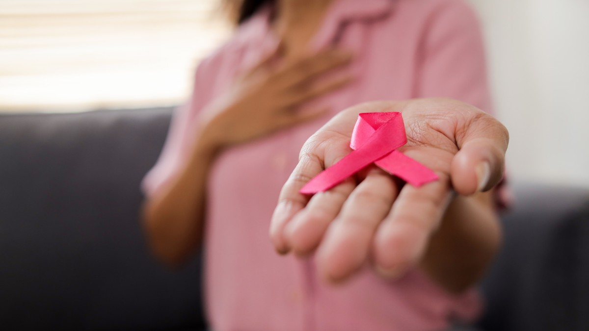 Mulher com camisa rosa segurando o laço rosa símbolo da campanha Outubro Rosa, representando conscientização e prevenção ao câncer de mama.